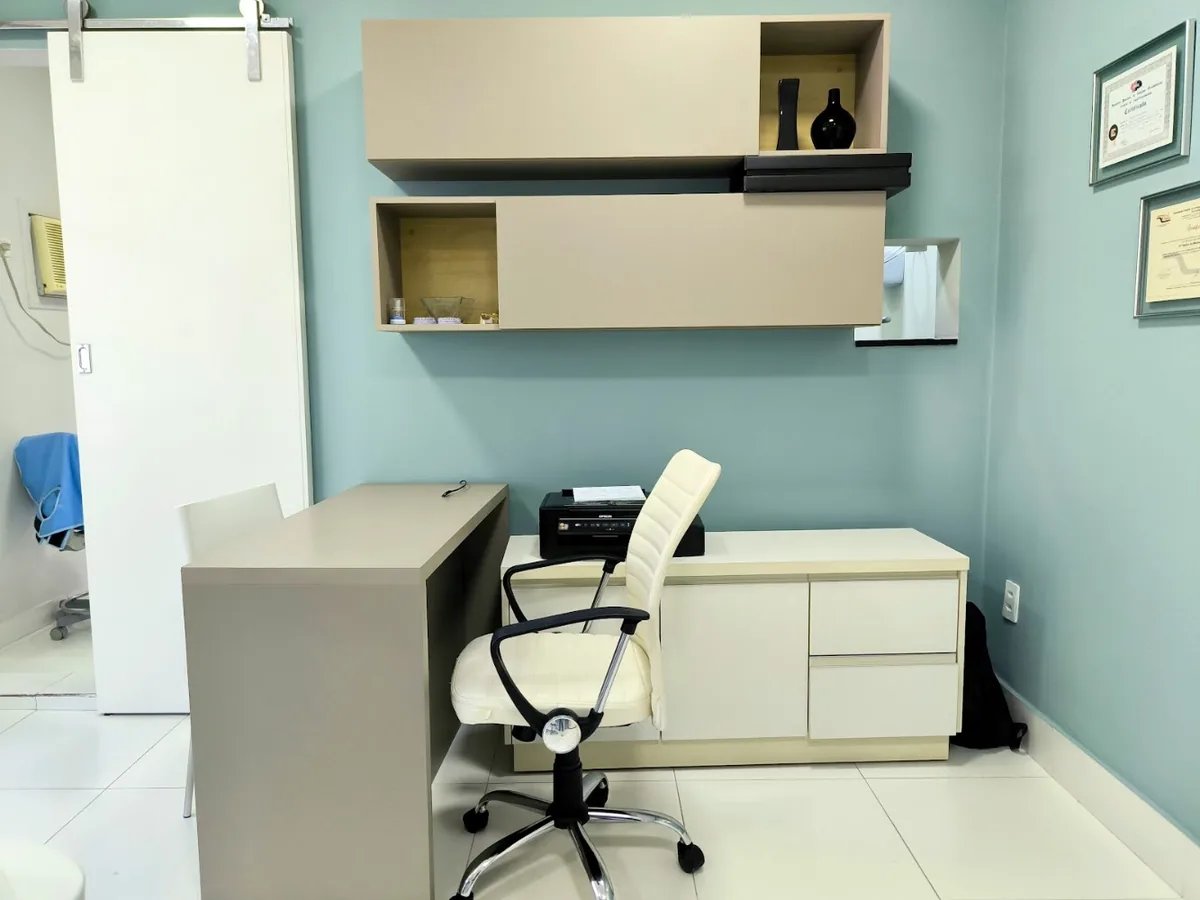 Sala clínica com parede verde-sálvia e mesa de madeira clara